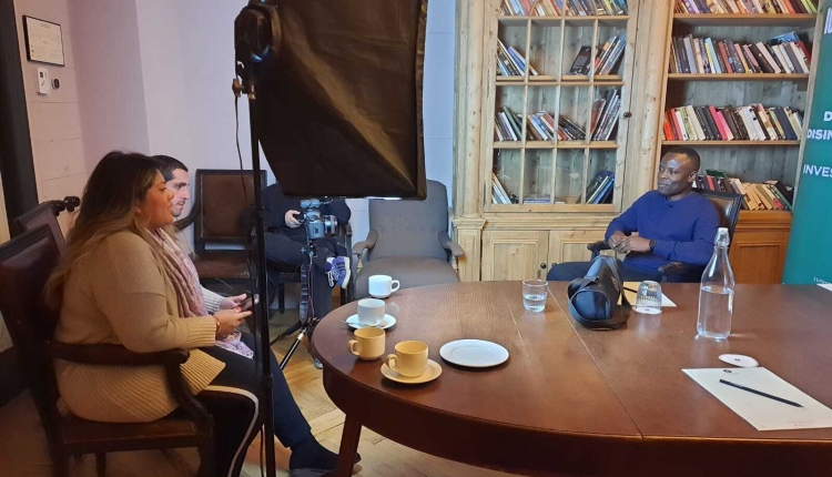 A photo of James Okong'o being interviewed in an office. He's sitting in front of a large light and camera equipment.
