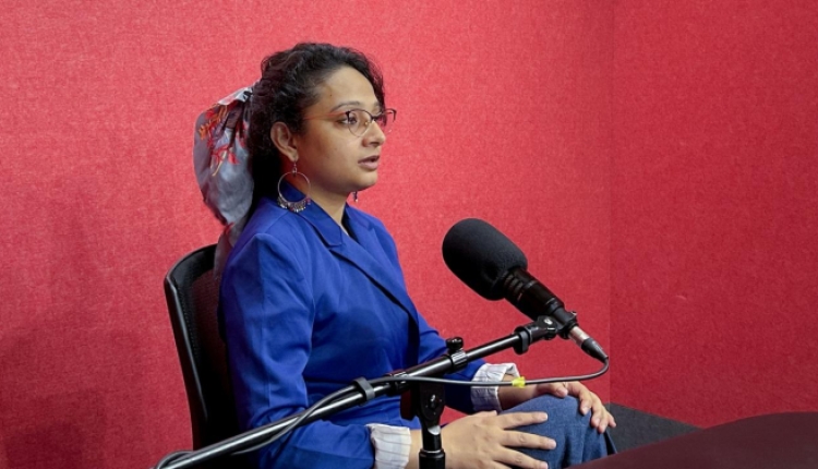 A photo of Jyoti sitting in a recording studio, with a microphone in front of her. 