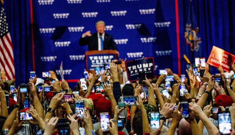 A photo of Donald Trump at a rally before the 2016 presidential election. He's standing at a podium with a crowd in front of him.